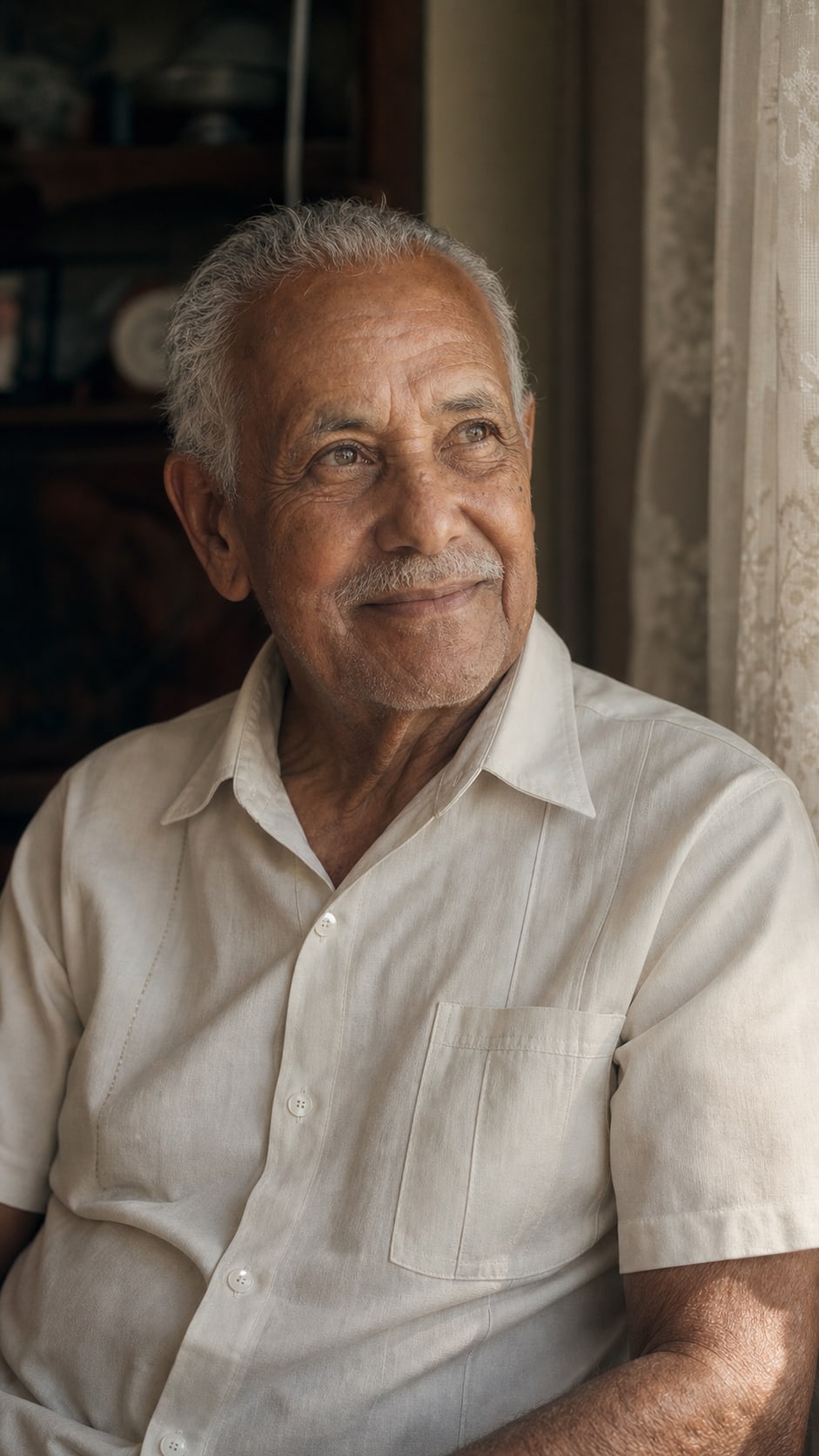 Senhor idoso sorrindo, sentado perto da janela de casa
